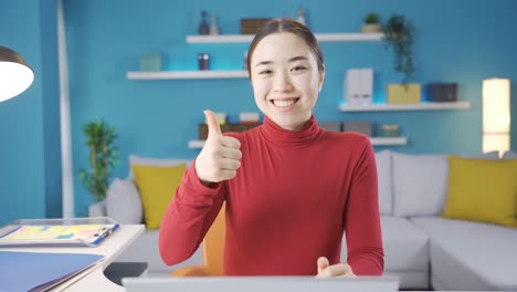 Asian-woman-is-pleased-with-what-she-sees-on-laptop-and-gives-a-positive-sign-to-the-camera.